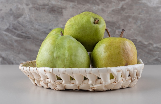 Bundle of pears in a white basket on marble 