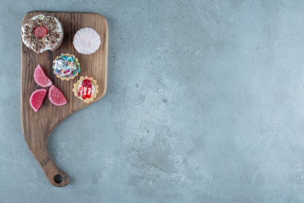 Bundle of various pastries and marmelades on a wooden board on marble background. High quality photo