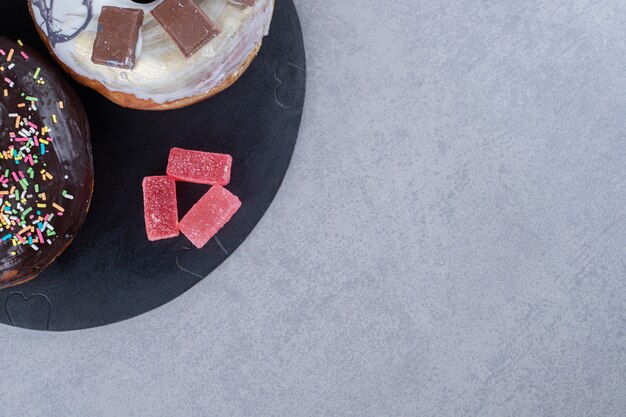 Bundled marmelades and two donuts on a tray on marble surface