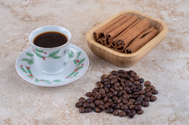 一杯のコーヒーの横にあるシナモンスティックとコーヒー豆の束