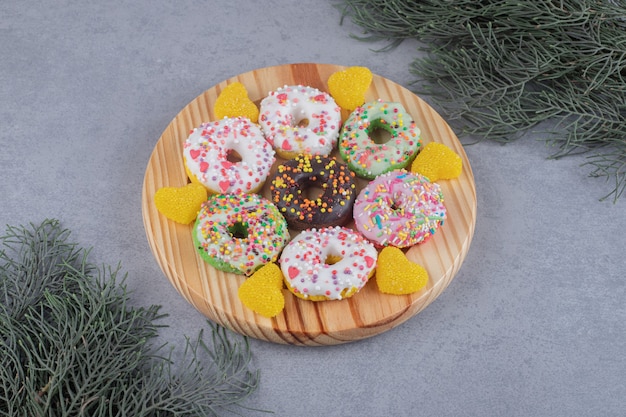 Bundles of pine branches next to donuts and marmelades on a platter on marble surface