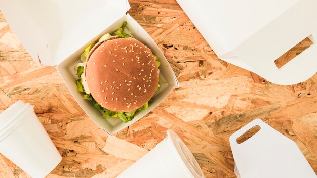 Burger in the box with packages on wooden backdrop