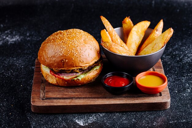 Burger bun, fried potatoes in a black bowl with ketchup and mustard.