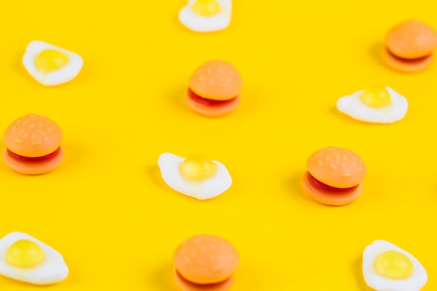 Burger candies and fried egg gummies on yellow surface