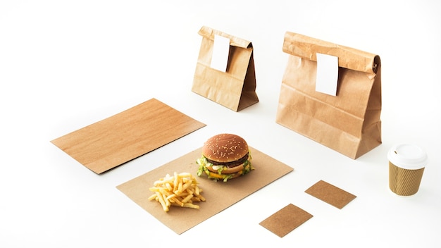 Burger and french fries on paper with disposable drink and paper package on white backdrop