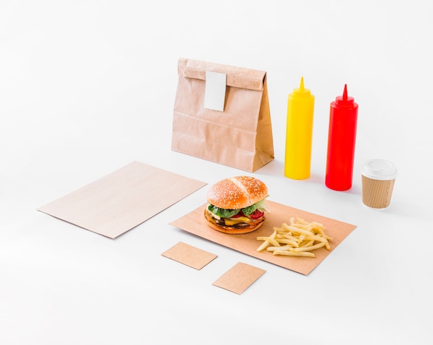 Foto gratuita burger; patatine fritte; pacco e bottiglia di salsa su sfondo bianco