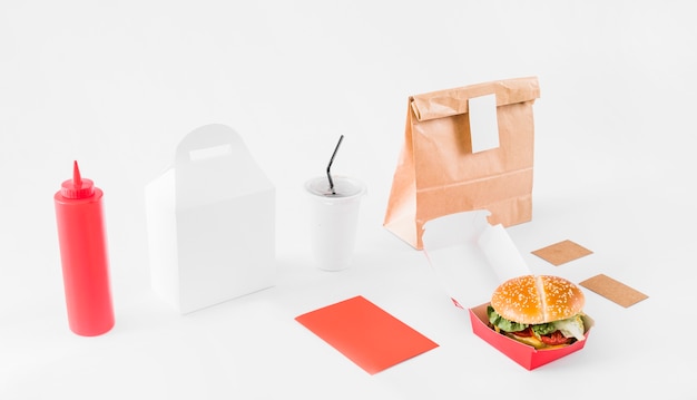 Burger; parcel; sauce bottle and disposal cup on white surface