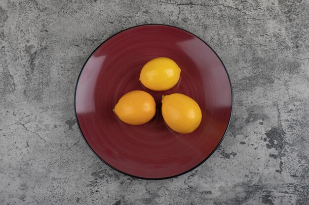 Free photo burgundy plate and fresh juicy lemons on stone table.