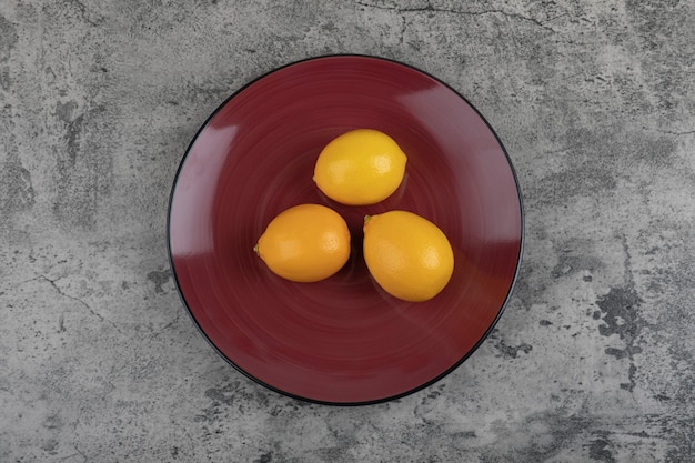 Burgundy plate and fresh juicy lemons on stone table.