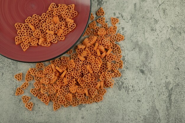 Burgundy plate of heart shaped raw macaroni on marble background