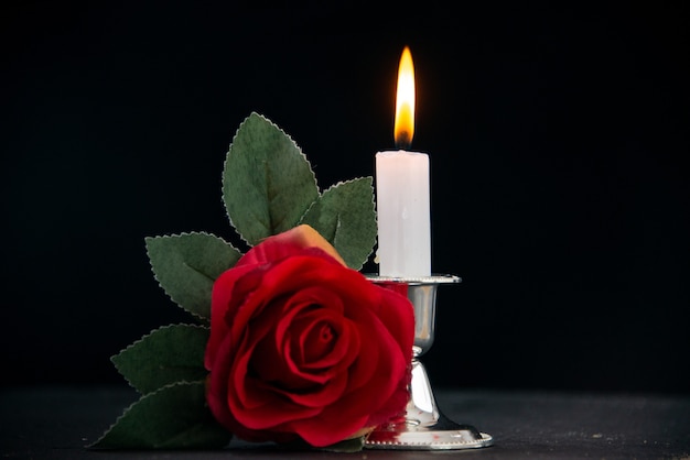 Burning candle with red flower as memory on a dark surface