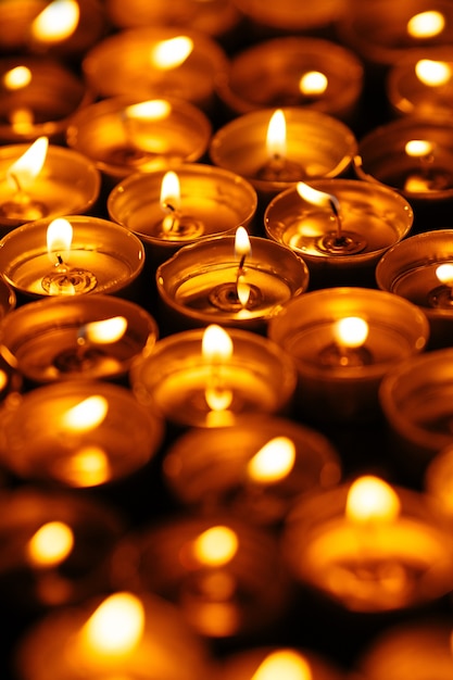  Burning candles. Many yellow candles glow in dark. Closeup