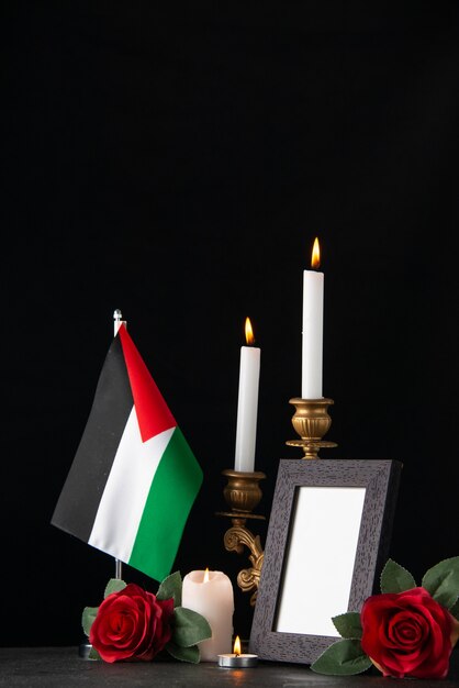 Burning candles with palestinian flag and flowers on a dark surface