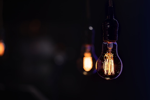 A burning lamp hangs in the dark on a blurred background.