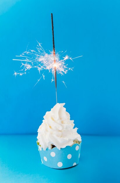 青い背景に対してクリーミーなカップケーキに線香花火を燃焼