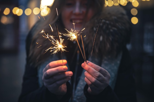 Burning sparklers in the hands of a young woman in the dark