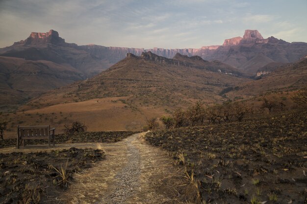 Burnt dry grass field in the desert with a narrow pathway and beautiful rocky mountains