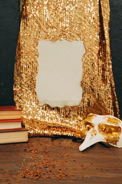 Burnt paper on golden sequin textile with carnival mask on wooden table