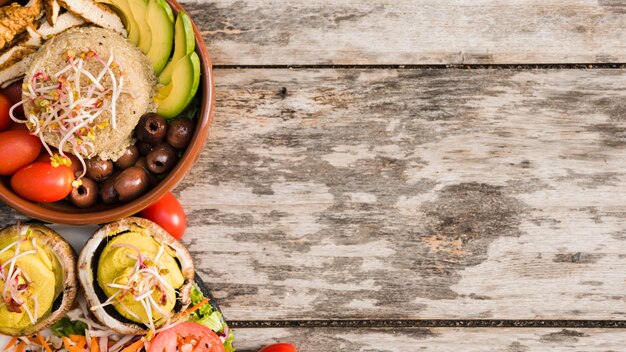 Burrito bowl with chicken; tomato; sprouts; olives and avocado slices in bowl with salad on wooden textured backdrop