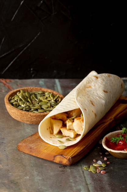 Burrito on wooden board near tomato sauce and cardamom