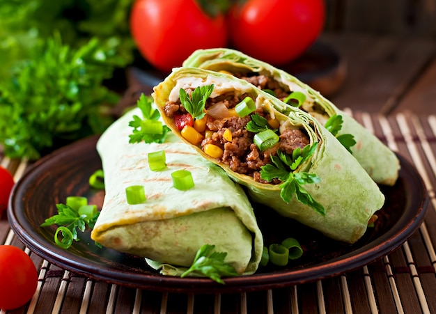 Burritos wraps with minced beef and vegetables on a wooden surface