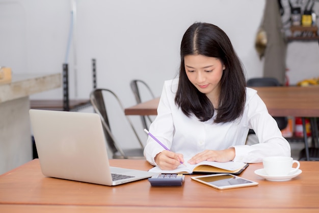 Business asian woman writing on notebook on table with laptop Premium Photo