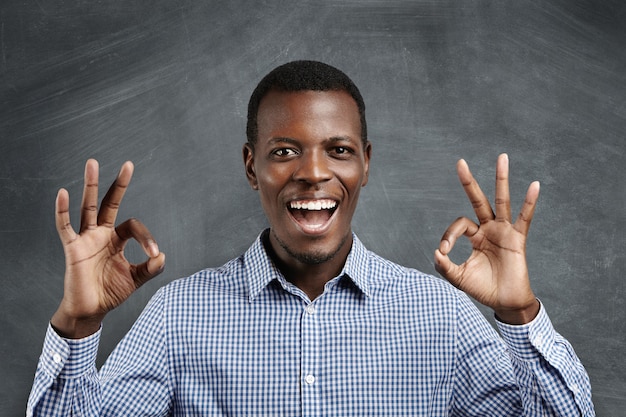 Business, carrier and success. young dark-skinned businessman having happy look, smiling, keeping his mouth wide open, gesturing, showing ok sign after concluding profitable deal. body language