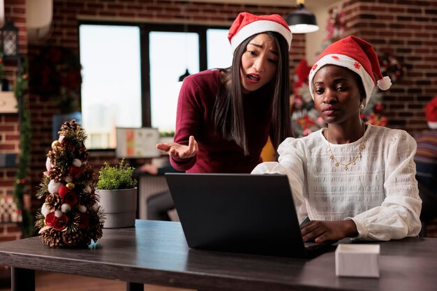 Business colleagues doing teamwork in festive office, brainstorming ideas to work on startup report. Working on laptop in workplace with christmas tree decorations and ornaments.