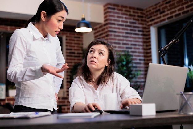 Business company employees in office workspace discussing about startup project marketing strategy. Multiethnic corporate workers analyzing management charts while using laptop.