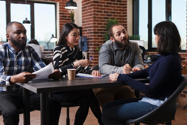 Free photo business company recruiting board sitting at desk in office while interviewing woman that came for vacant job. multiethnic recruiters talking with candidate about available post details.