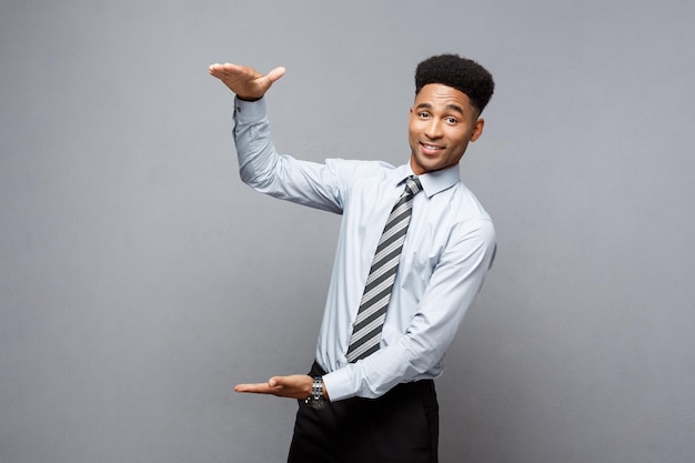 Business Concept Amazed African American holding both hands on side presenting projects over grey background