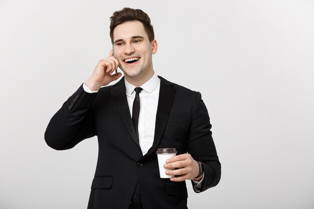 ビジネスコンセプト：クローズアップ自信を持って若いハンサムなビジネスマンが携帯電話で話し、白い孤立した背景でコーヒーを飲みます。