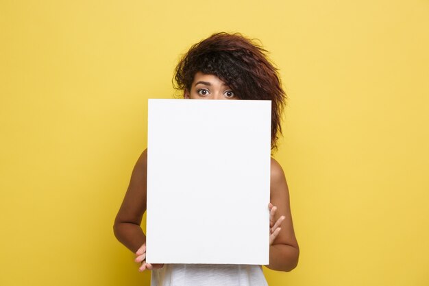 Business Concept - Close up Portrait young beautiful attractive African American smiling showing plain white blank sign. Yellow Pastel studio Background. Copy space.