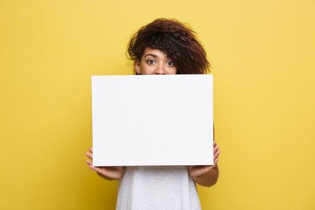 Business Concept - Close up Portrait young beautiful attractive African American smiling showing plain white blank sign. Yellow Pastel studio Background. Copy space.