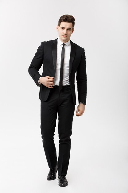 ビジネスコンセプト：白い背景の上を歩くスマートスーツを着たエレガントなビジネスマンの完全な長さの肖像画の写真。