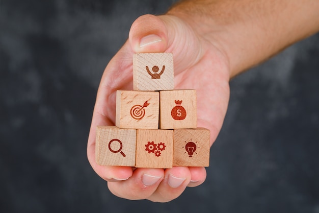 Free photo business concept on grungy grey table side view. hand holding wooden blocks with icons.