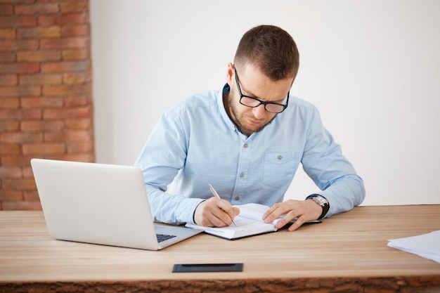 Business concept. mature unshaven male director of company in glasses and blue shirt working in office