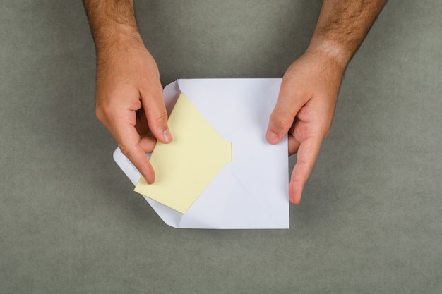 Бесплатное фото Бизнес-концепция на серой поверхности плоской планировки. человек берет письмо из конверта.