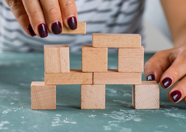 Free photo business concept side view. woman building up tower from wooden blocks.