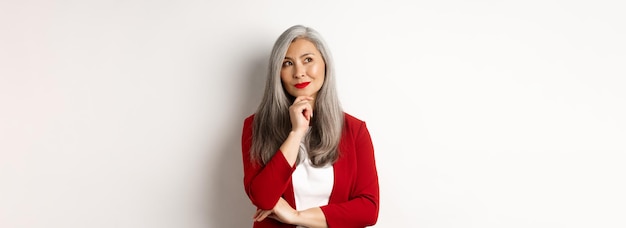 Free photo business concept smiling mature lady in red blazer smiling and looking satisfied while thinking stan