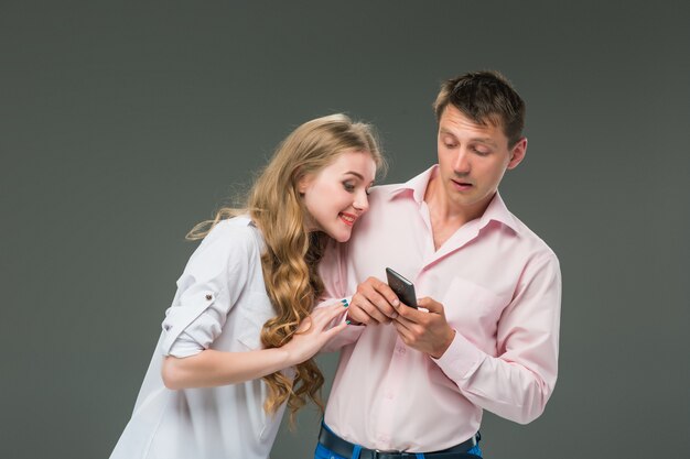 Business concept. The two young colleagues holding mobile phones on gray wall