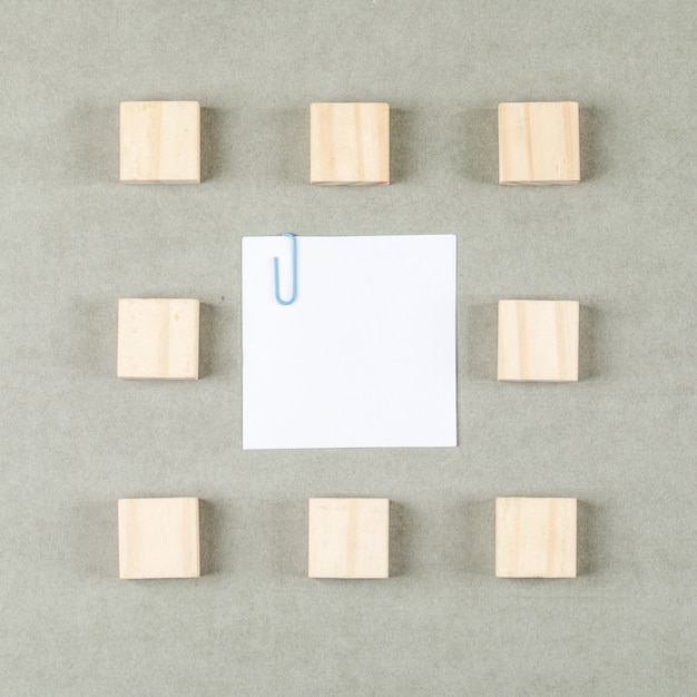 Free photo business concept with clipped sticky note, wooden blocks on grey surface flat lay.