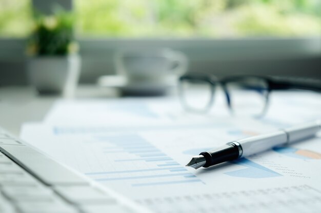 Business concept with copy space. Office desk table with pen focus and analysis chart, computer, notebook, cup of coffee on desk.Vintage tone Retro filter, selective focus.