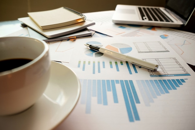 Business concept with copy space. Office desk table with pen focus and analysis chart, computer, notebook, cup of coffee on desk.Vintage tone Retro filter, selective focus.