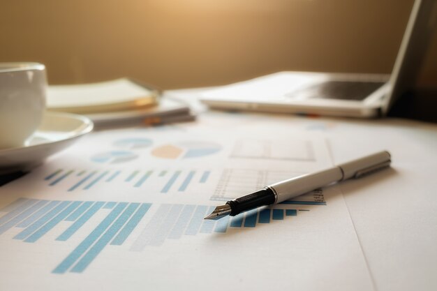 Business concept with copy space. Office desk table with pen focus and analysis chart, computer, notebook, cup of coffee on desk.Vintage tone Retro filter, selective focus.