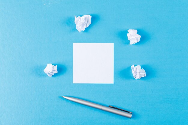 しわくちゃの紙の塊、付箋、平らな青色の背景にペンのビジネスコンセプトを置きます。