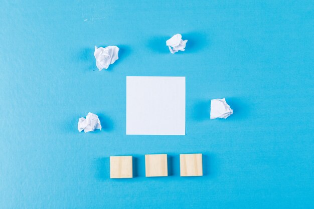 Business concept with crumpled paper wads, sticky note, wooden cubes on blue background flat lay.