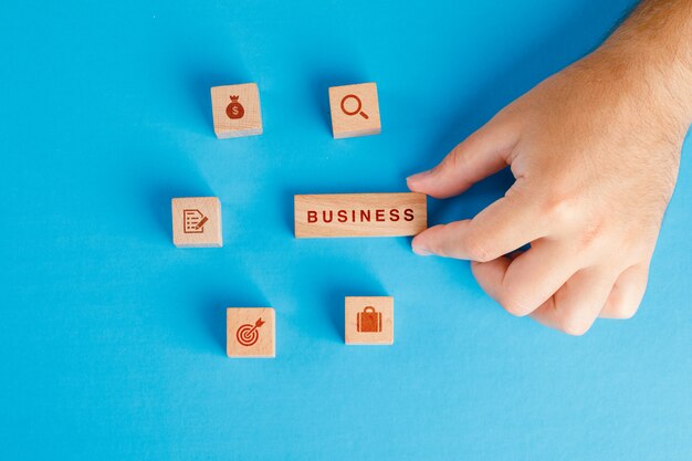 Бизнес-концепция с иконами на деревянных кубиков на синем столе плоской планировки. рука держит деревянный блок.