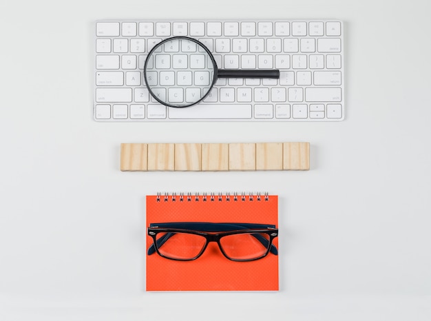 Free photo business concept with wooden blocks, glasses, magnifying glass on keyboard on white background flat lay.