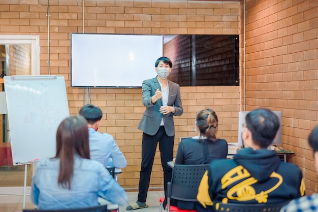 비즈니스 협력:젊은 아시아 남성 코치나 연사는 사무실 회의에서 다양한 사업가들에게 플립 차트 프레젠테이션을 합니다. 남성 교사 또는 트레이너는 다양한 동료에게 프로젝트를 제시합니다.
